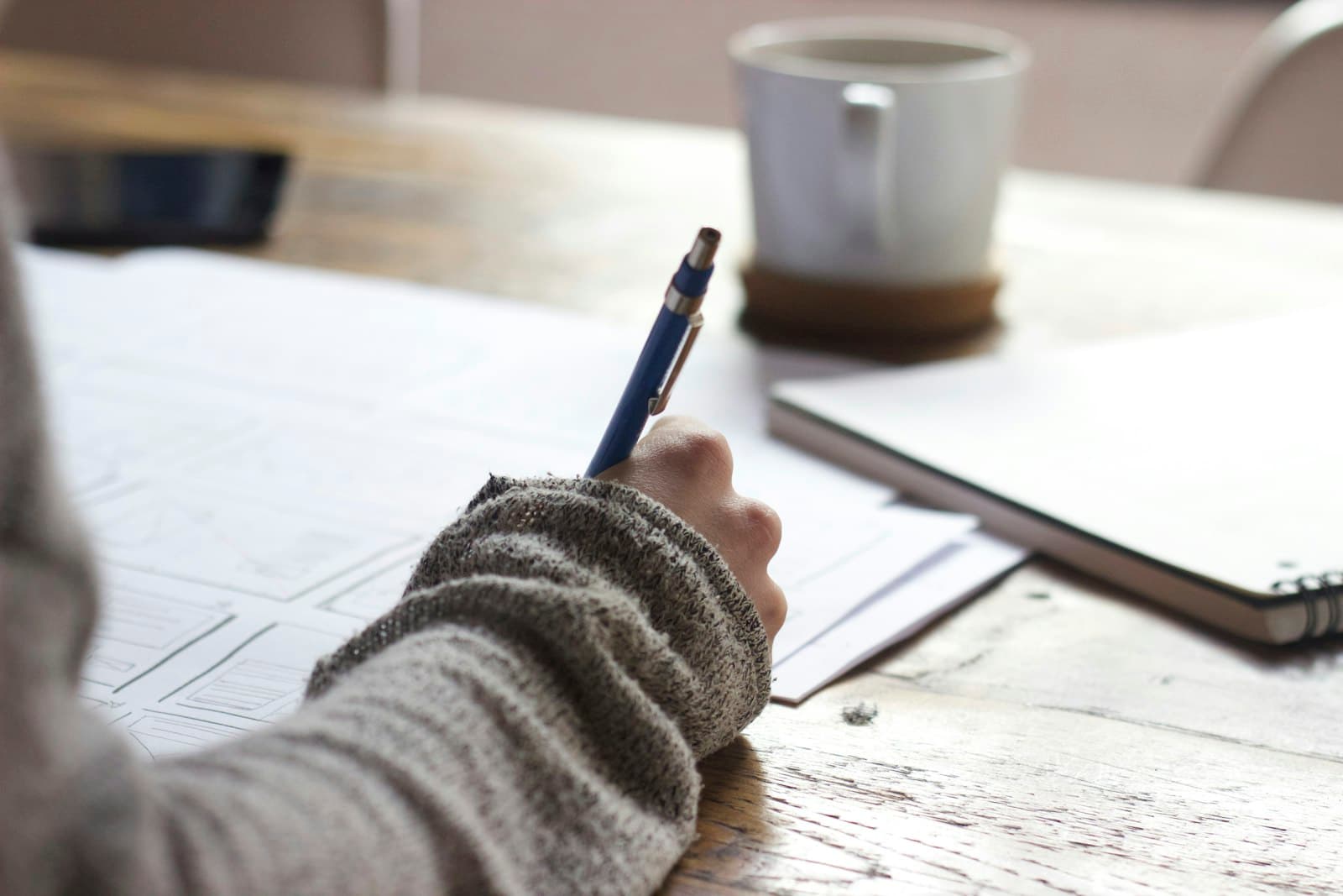 A researcher writing by hand at a wooden desk